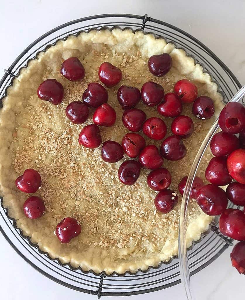 Filling tart crust with fresh cherries, white surface