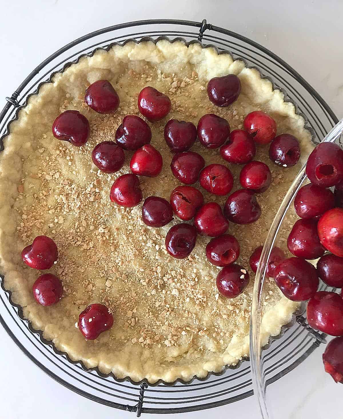 Filling tart crust with fresh cherries, white surface.