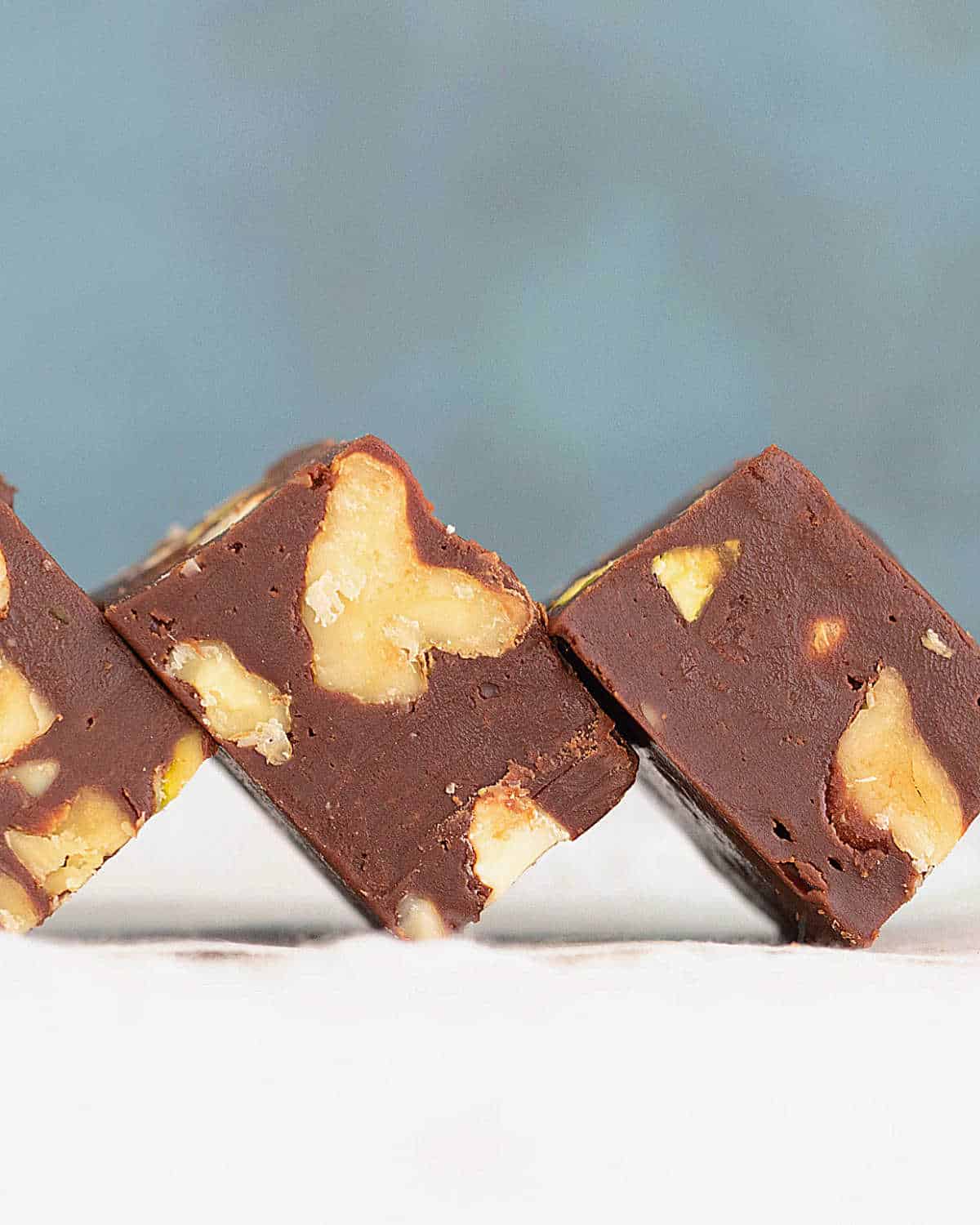 Close up of chocolate walnut fudge pieces on a white surface with a blue background.