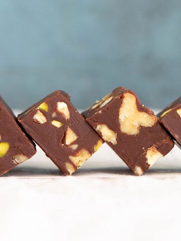 White surface and blue background with squares of chocolate nut fudge leaning into each other.