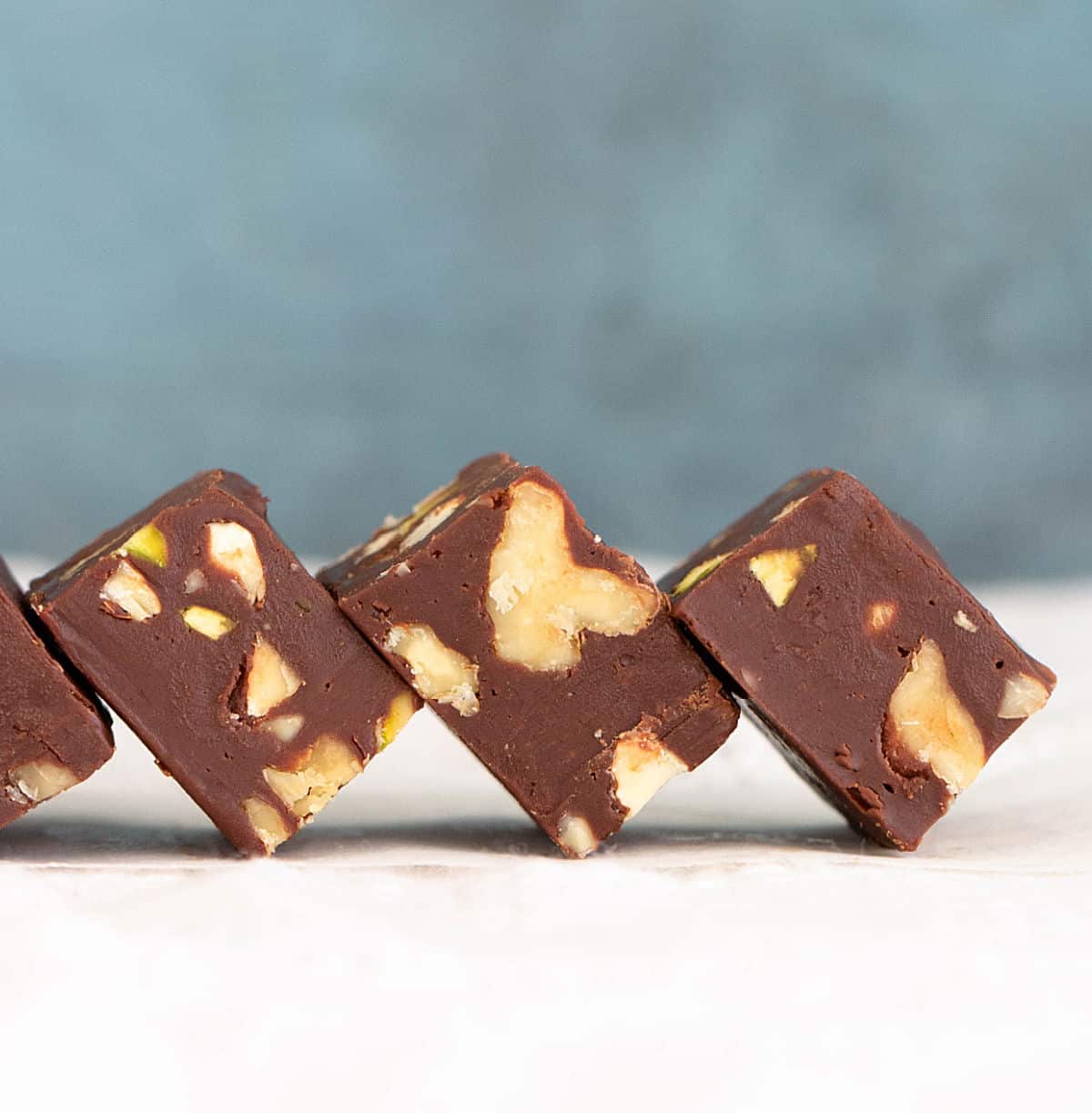 Row of leaning pieces of chocolate walnut squares with blue background and a white surface.
