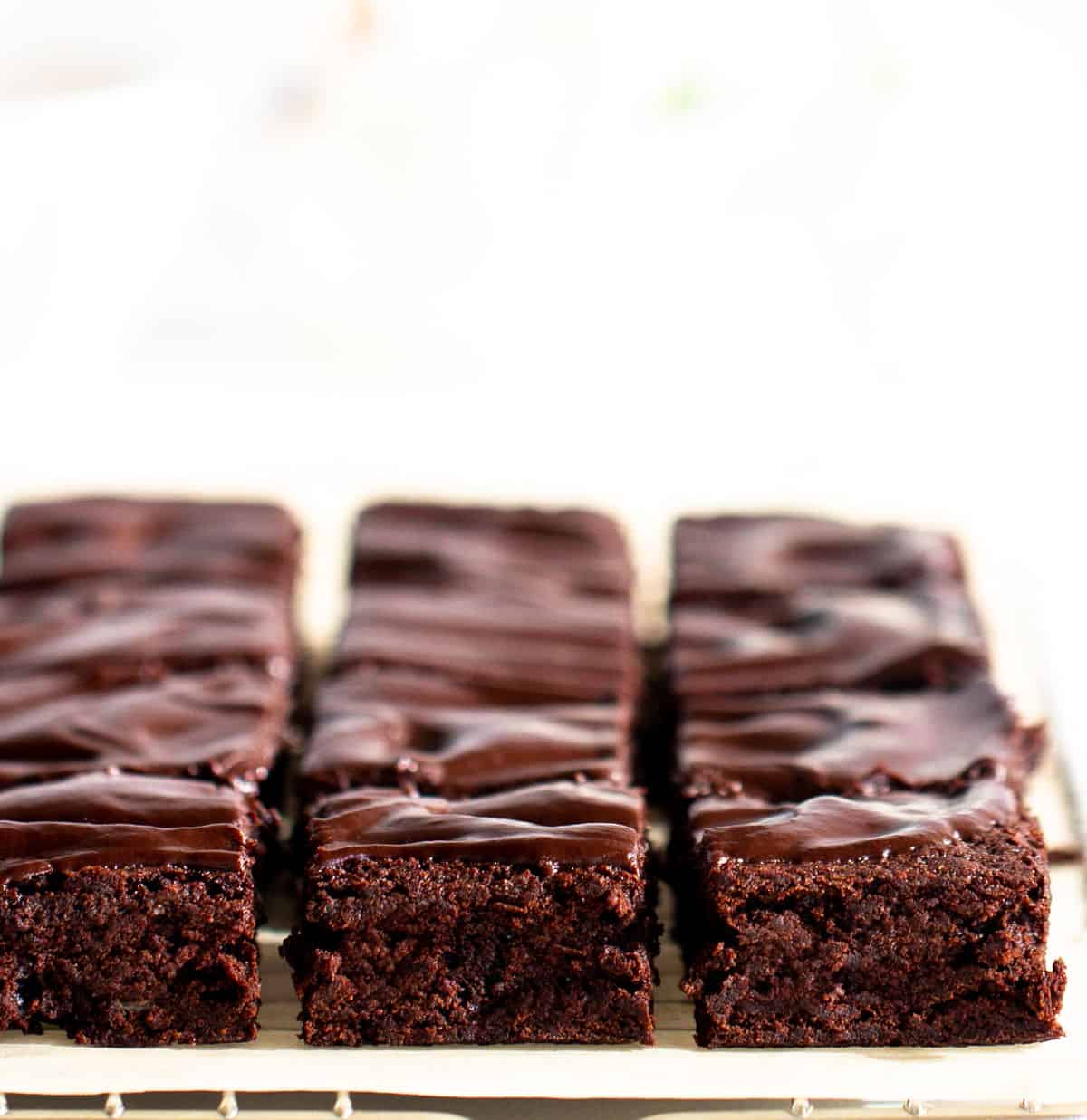 Brownie squares with ganache on top on parchment paper and wire rack