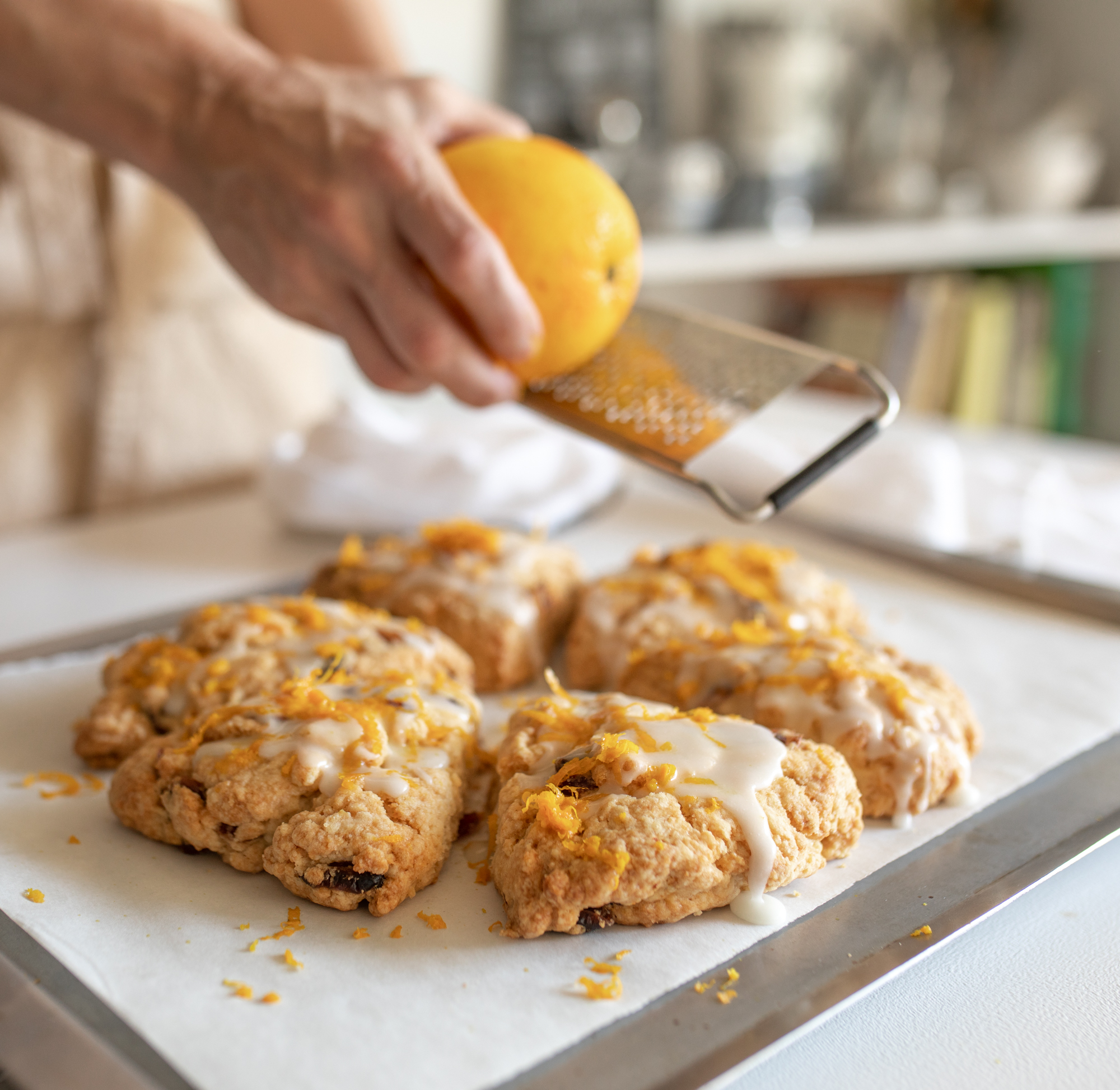 Grating orange peel over glazed scones on white table