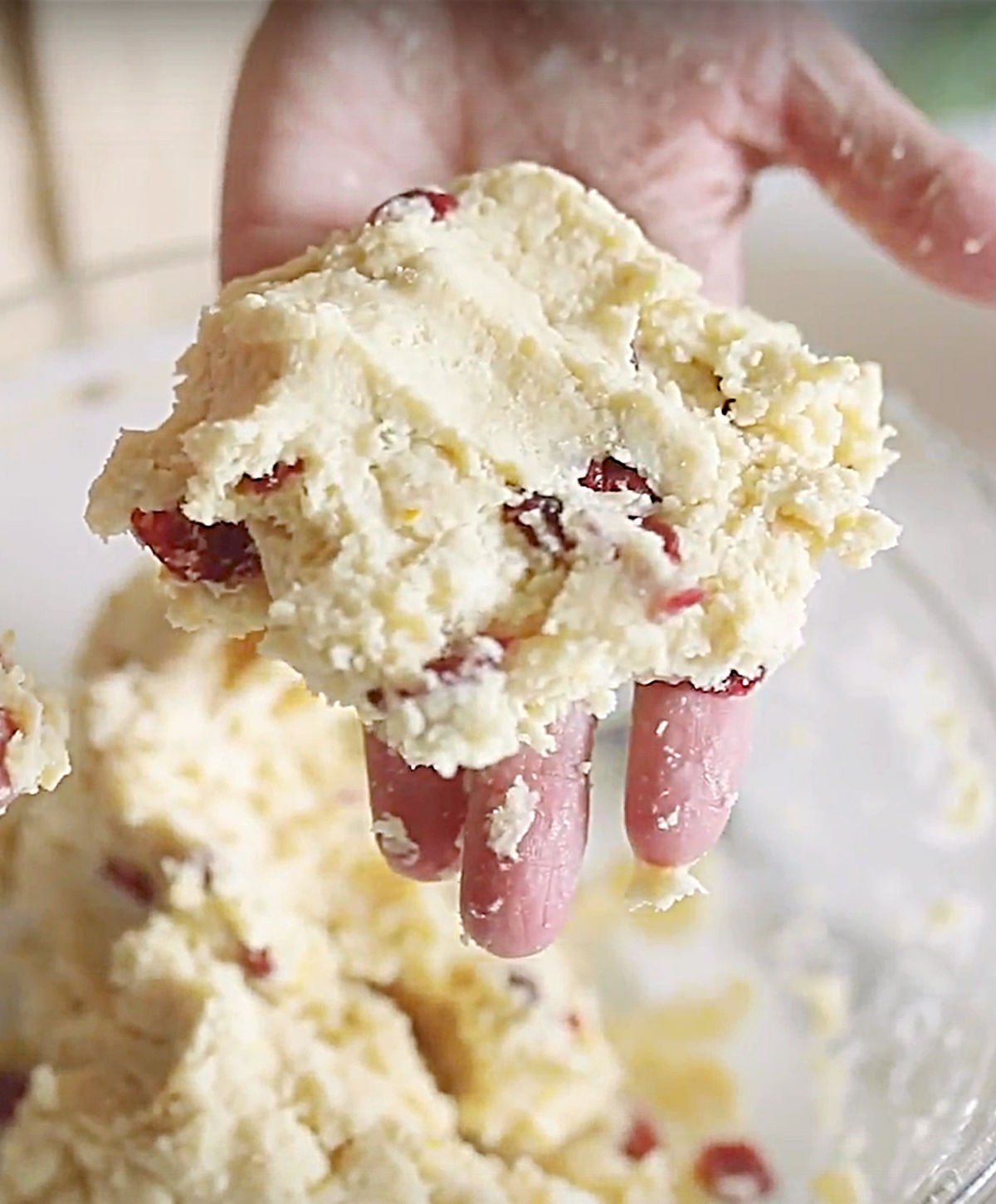 Hand holding piece of cranberry scone dough.
