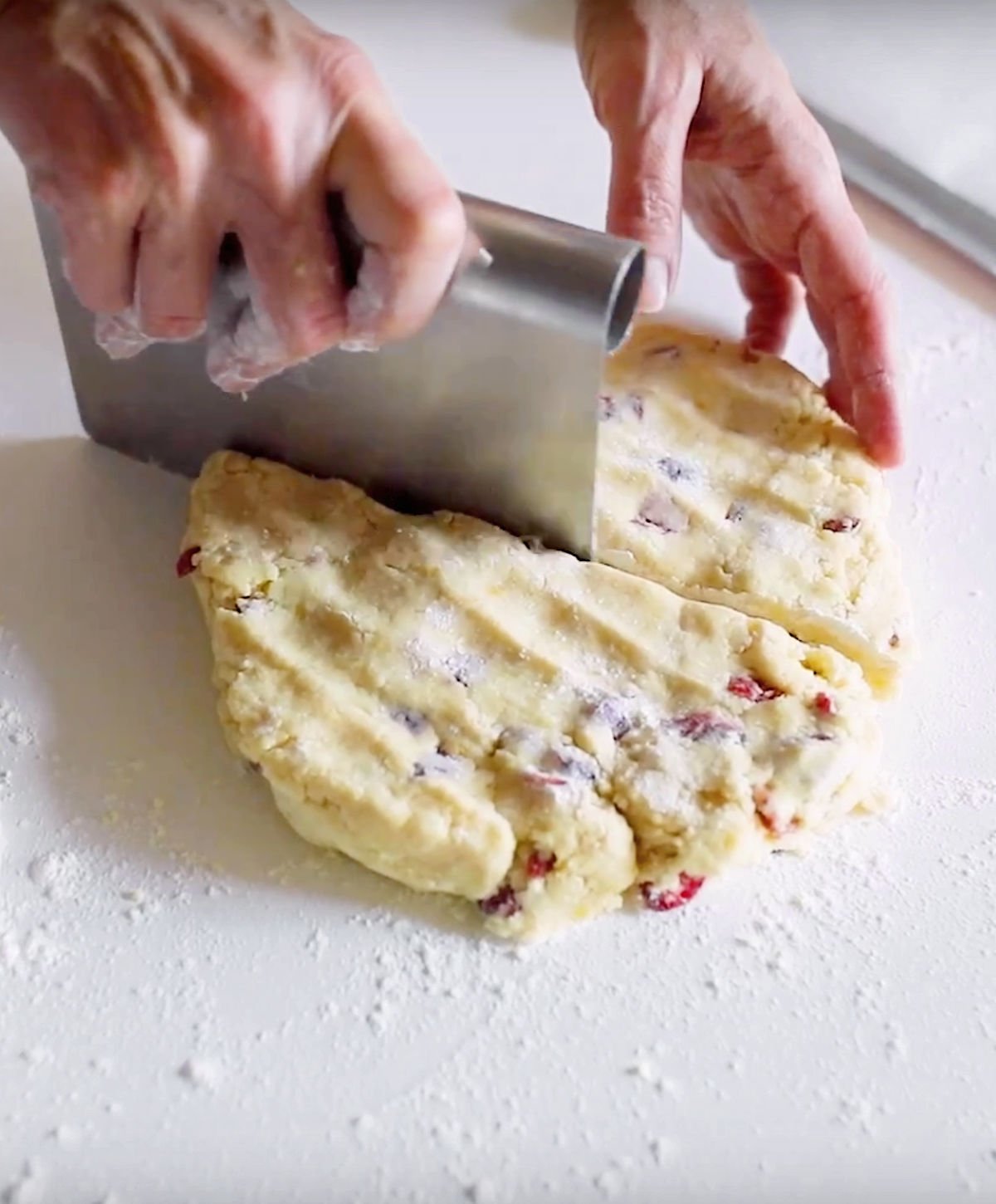 Cutting circle of cranberry scone dough on a white surface with a dough scraper.
