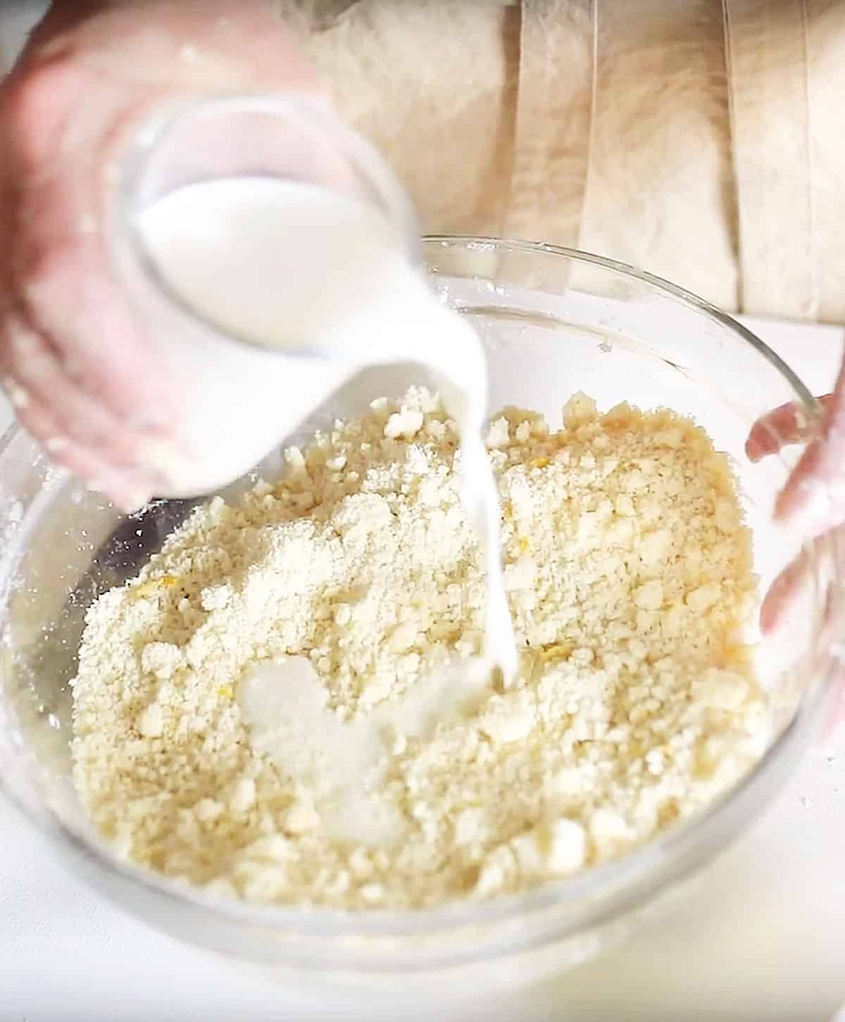 Adding milk to buttery scone dough in a glass bowl.