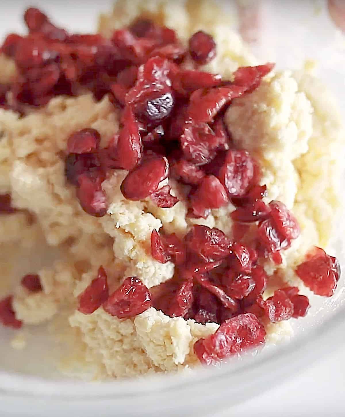 Dried cranberries added to scone dough in a glass bowl. Close up image.