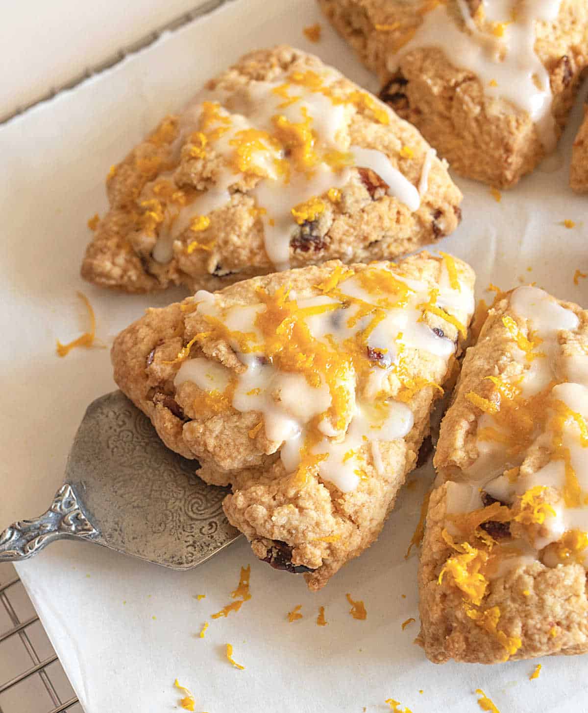 Half circle of glazed orange cranberry scones triangles on parchment paper with a cake server.