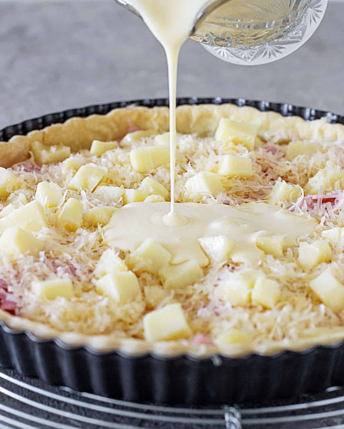 Pouring binding cream over ham and cheese quiche. Grey background.