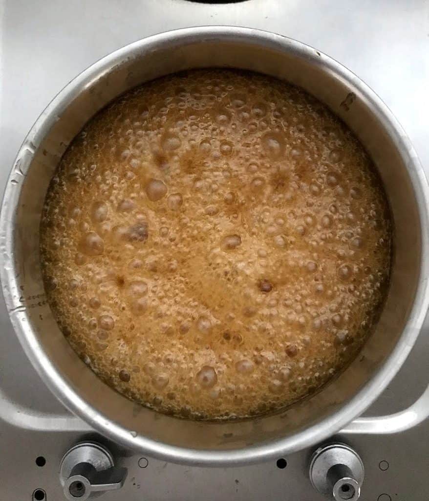 Honey mixture bubbling in a metal saucepan on a metal stove.