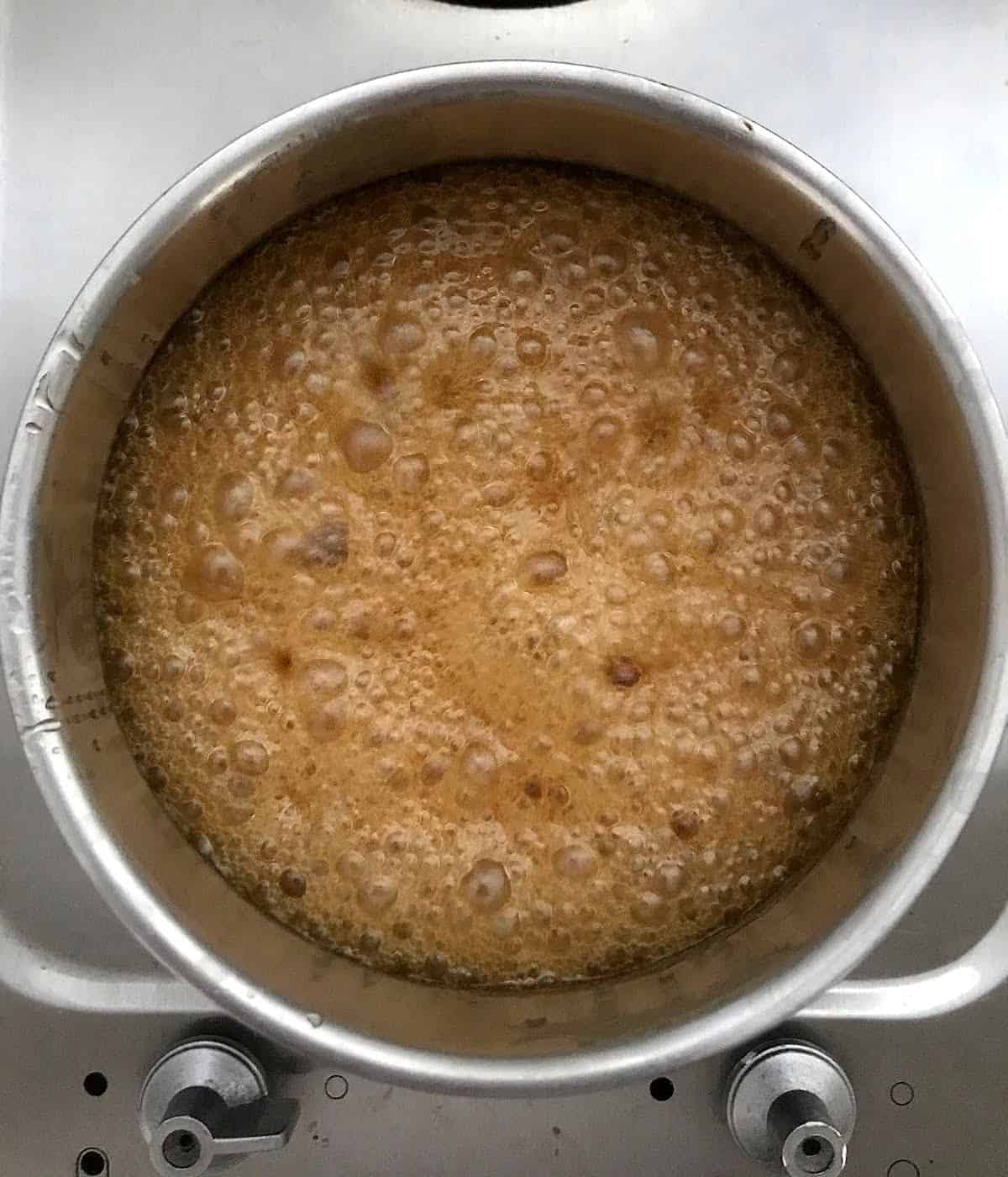 Honey mixture bubbling in a metal saucepan on a metal stove.