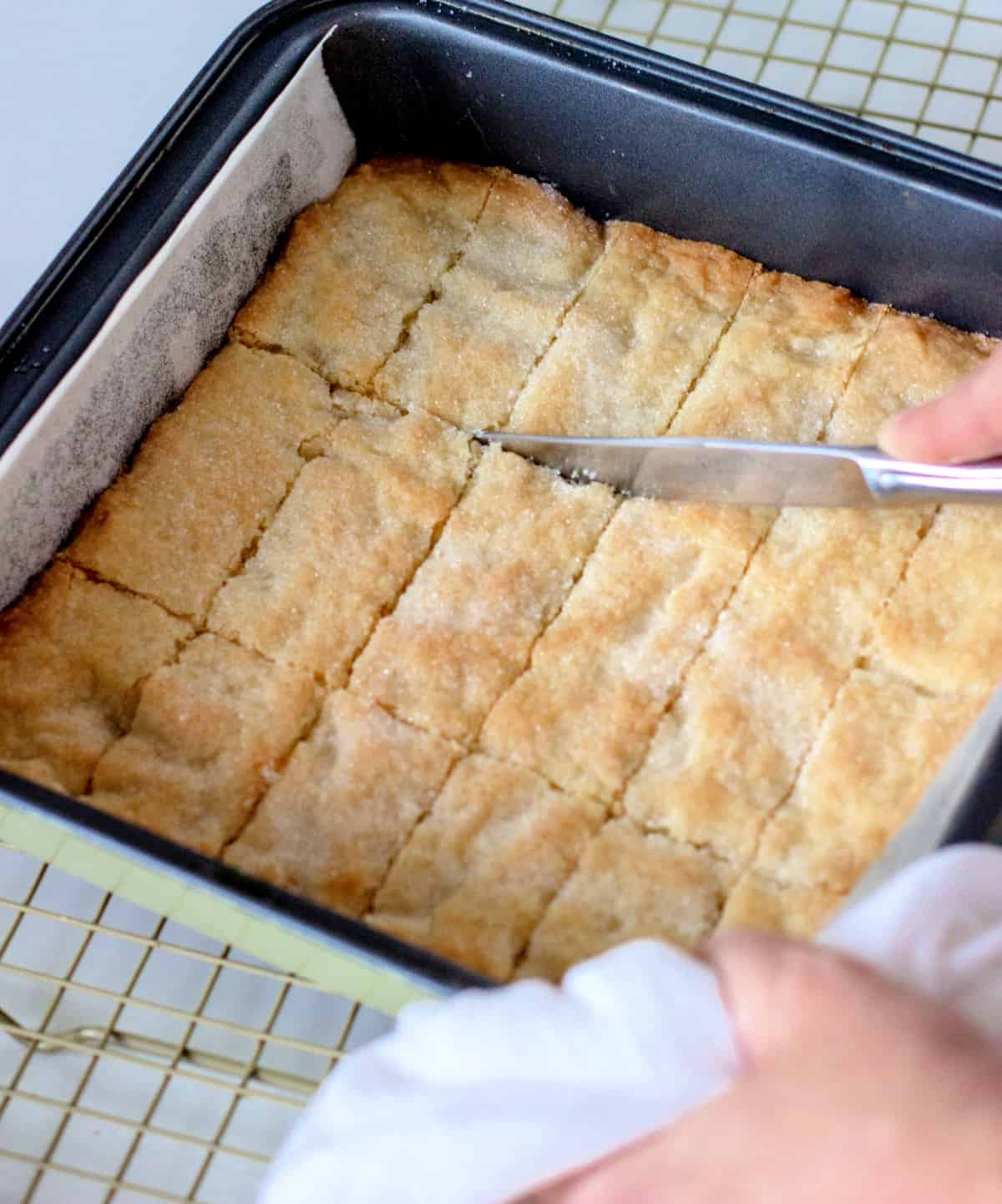 Cutting baked shortbread with a knife in the metal square pan.