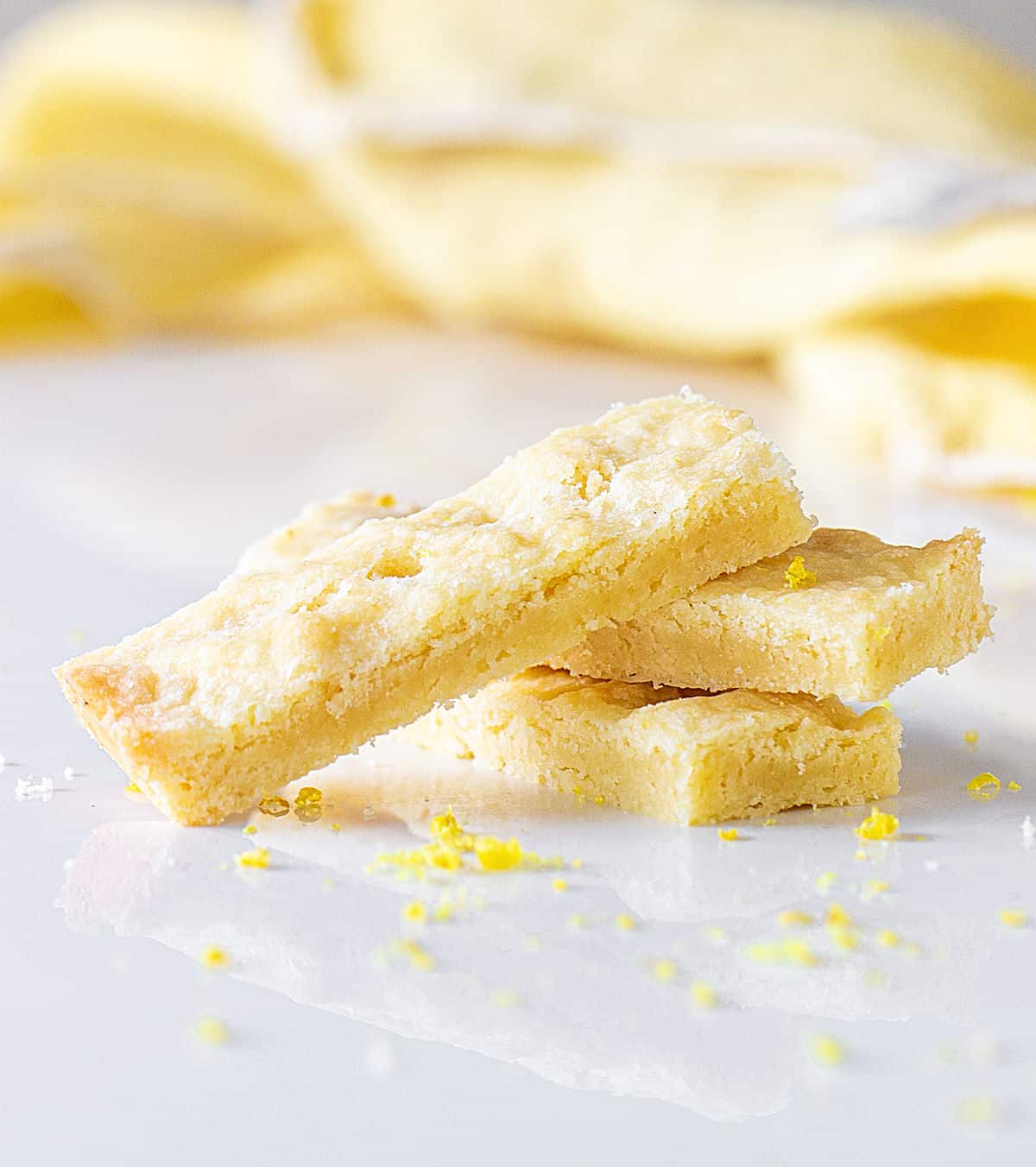 Stack of lemon shortbread fingers on white marble surface. Yellow cloth in background. 