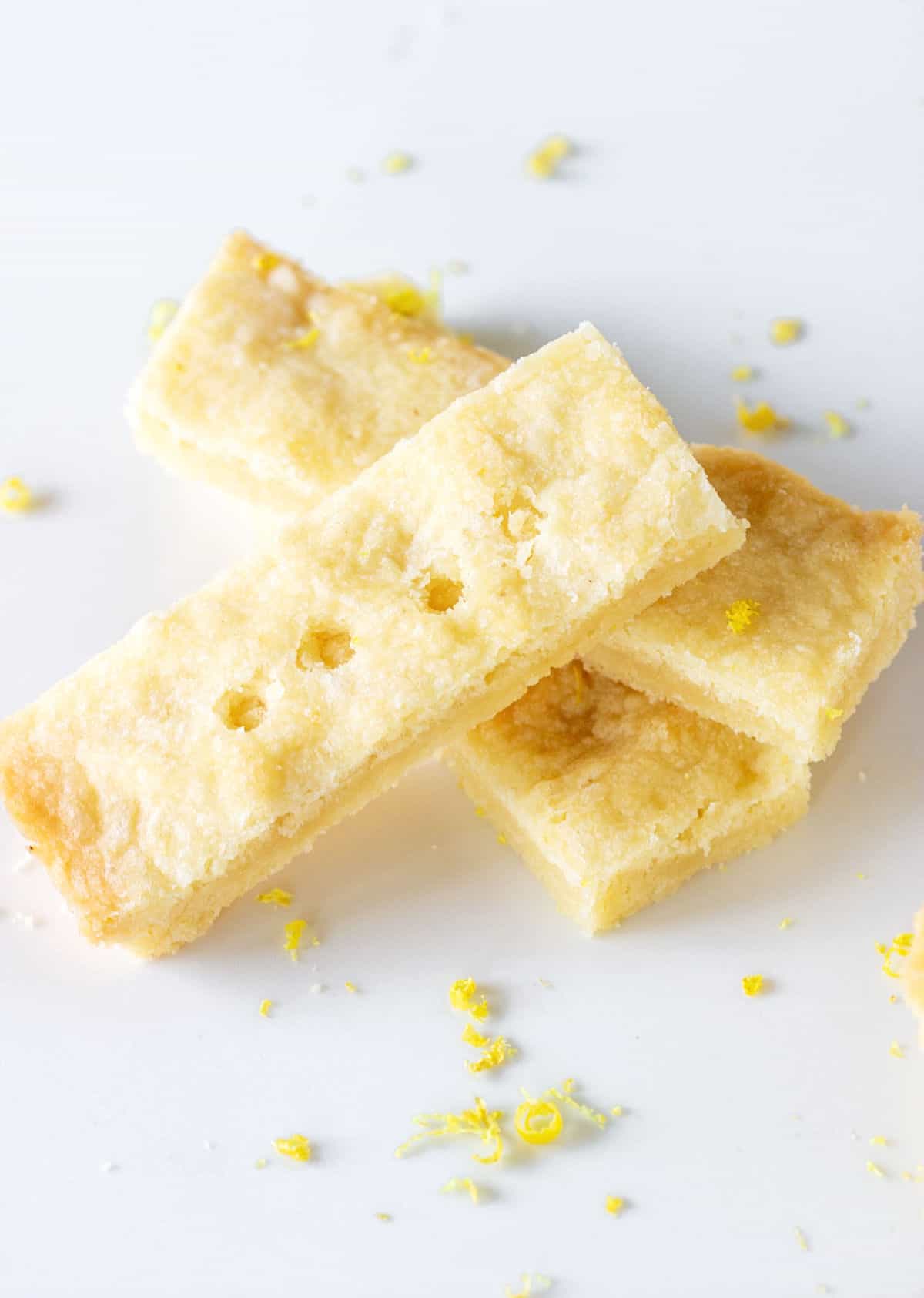Top view of three lemon shortbread pieces on white marble surface. Lemon zest around.