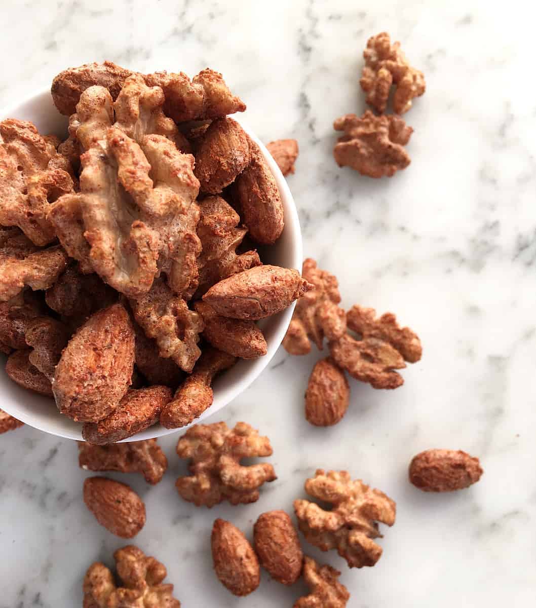 Cocktail nuts in a white bowl on a white marble surface.