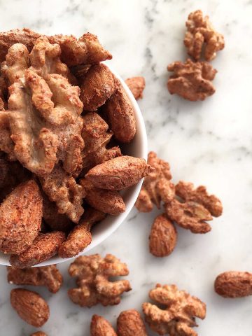 Cocktail nuts in a white bowl on a white marble surface.