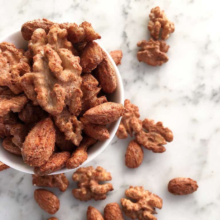 Cocktail nuts in a white bowl on a white marble surface.