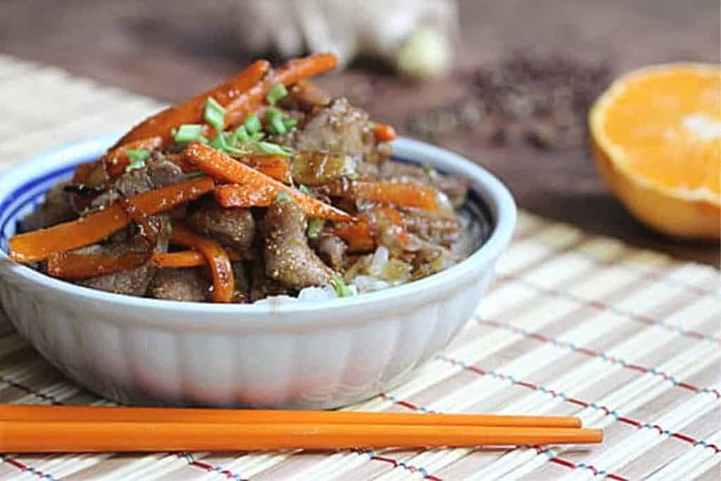 White bowl with pork and carrot dish, orange chopsticks, bambu placemat