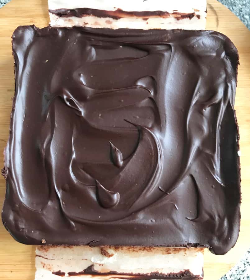 Chocolate topped square cake out of the fridge on a wooden counter.