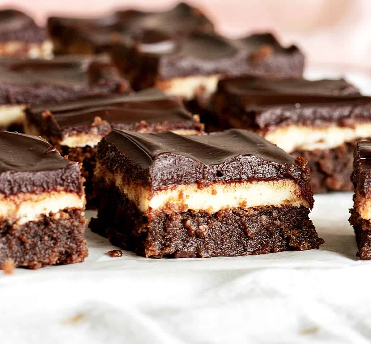Close-up image of triple layer chocolate squares on a white surface