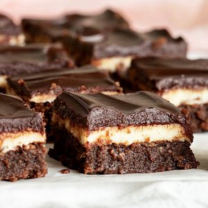 Squares of triple brownie cake on white surface, pink background.