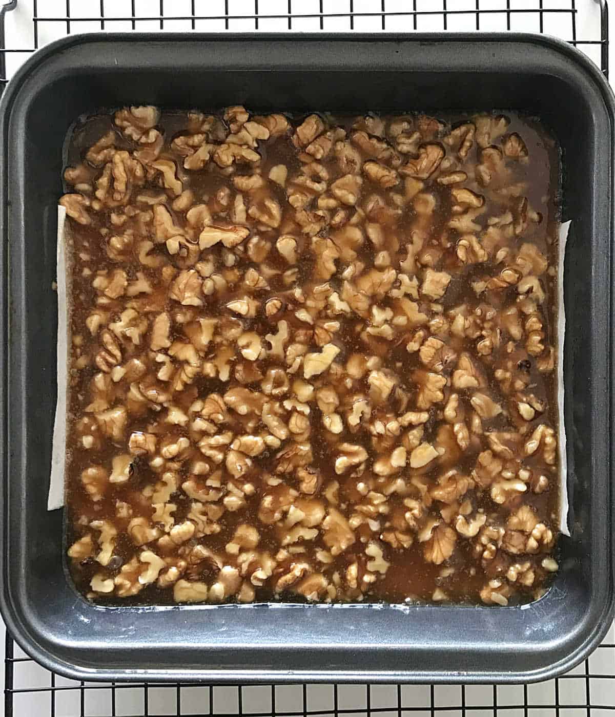 Black rack with square baking pan containing unbaked honey walnut squares.