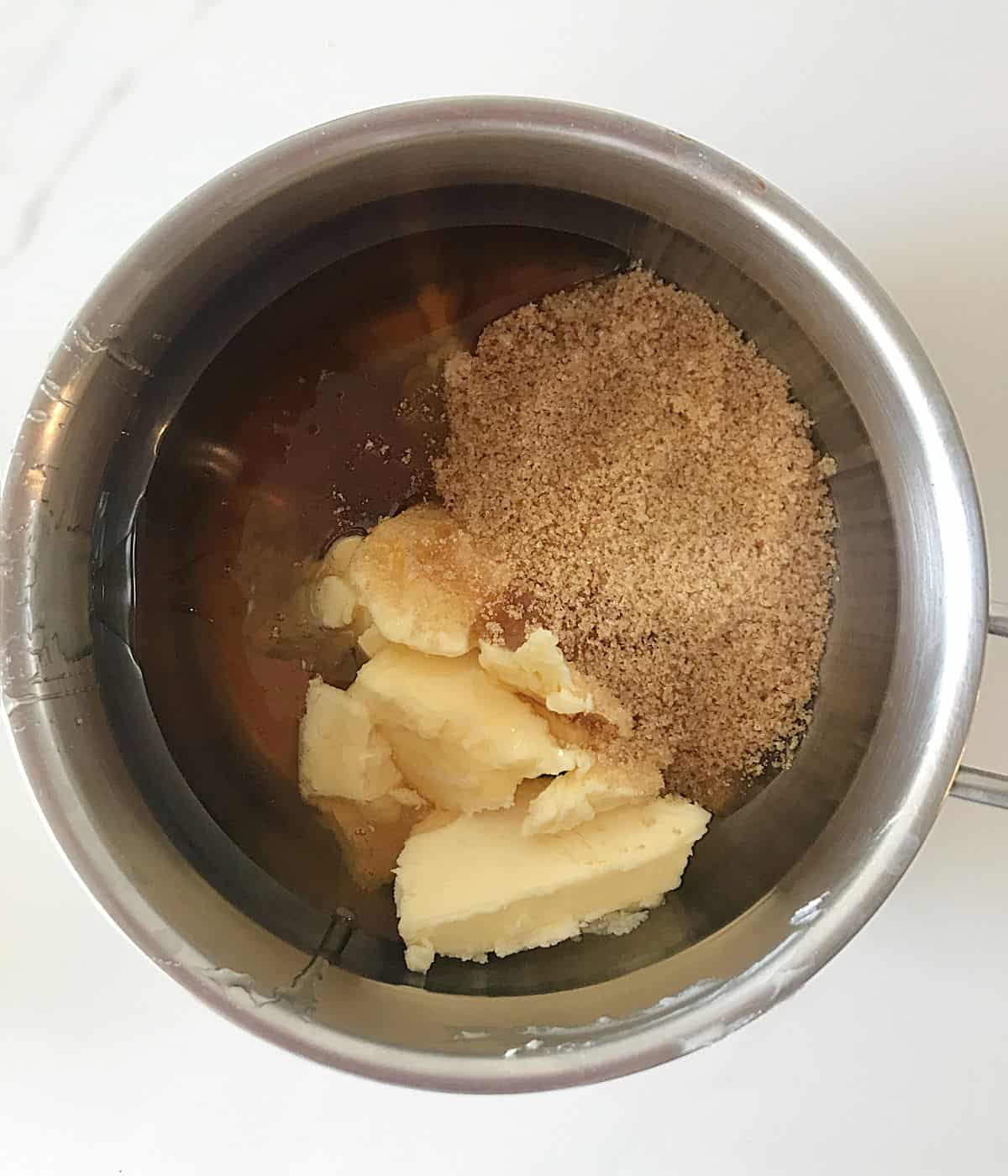 Butter, brown sugar, and honey in a metal saucepan on a white surface.