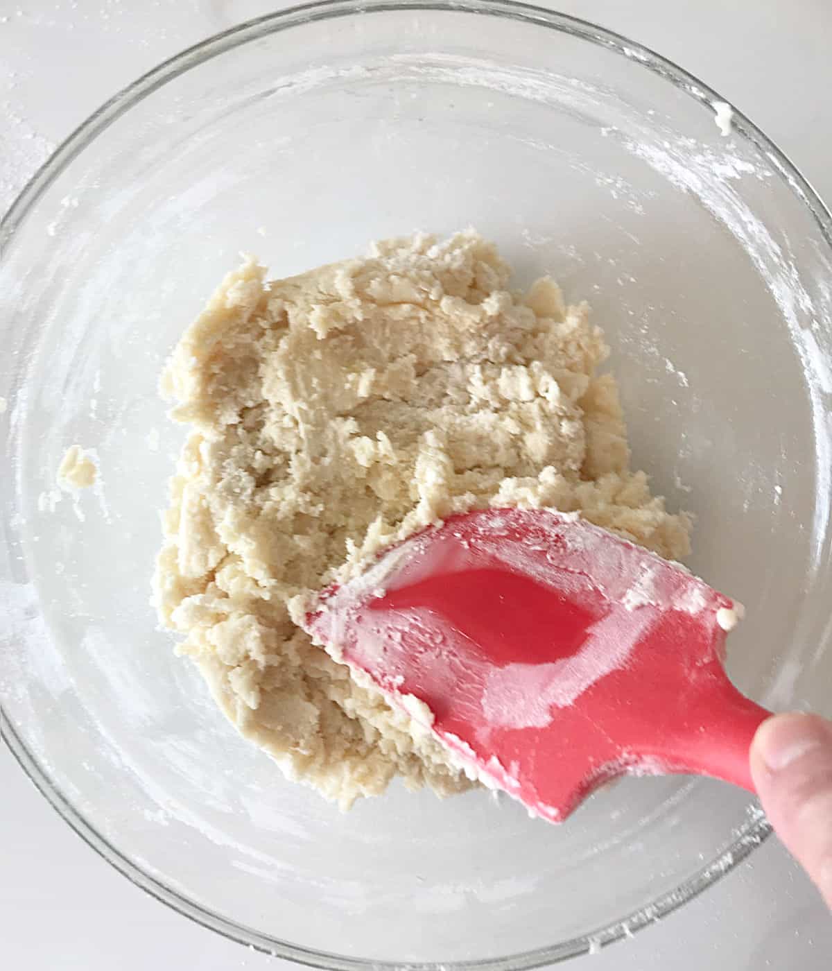 Red spatula mixing butter and sugar in a glass bowl on a white surface.