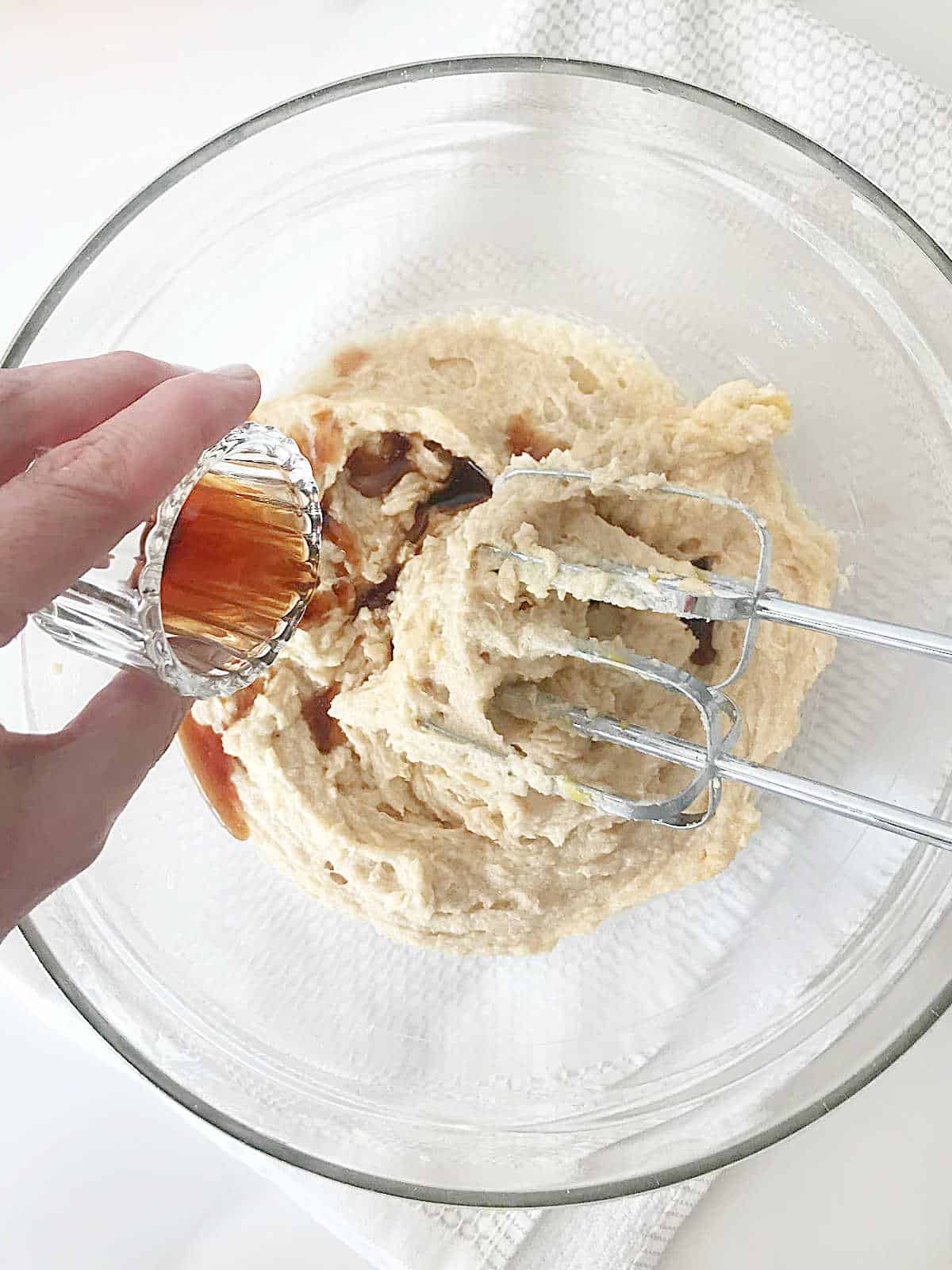 Adding vanilla to blondie dough in a glass bowl on a white surface.