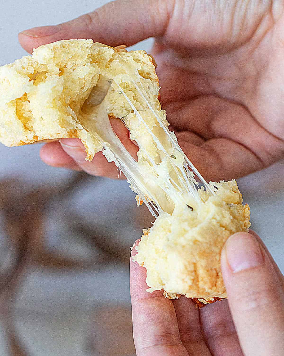Hands pulling apart scone, cheesy strands