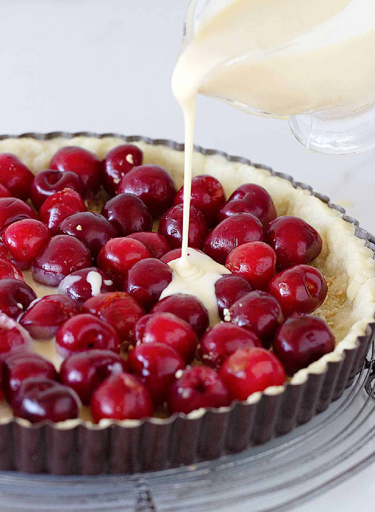 Pouring custard filling over fresh cherries in tart pan.