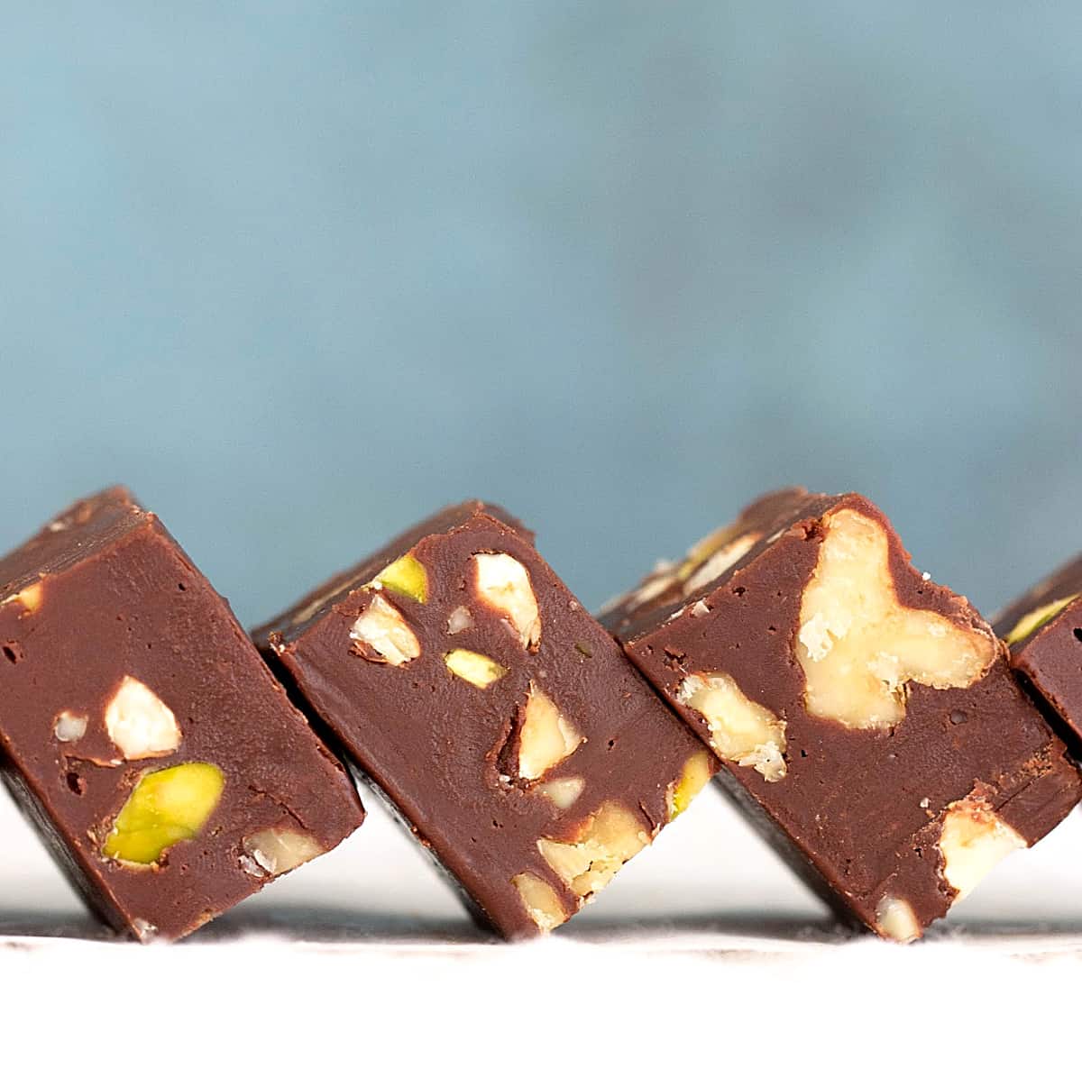 Squares of chocolate fudge with add-ons, white surface and blue background