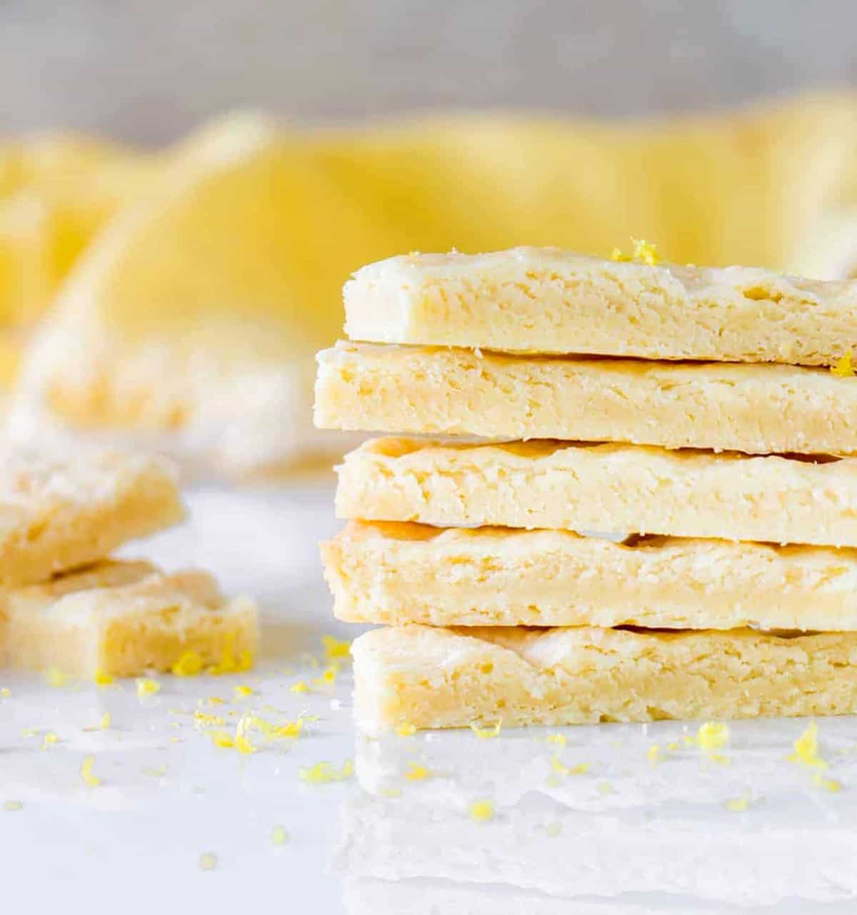 Five lemon shortbread fingers stacked on a white marble surface. Yellow background.