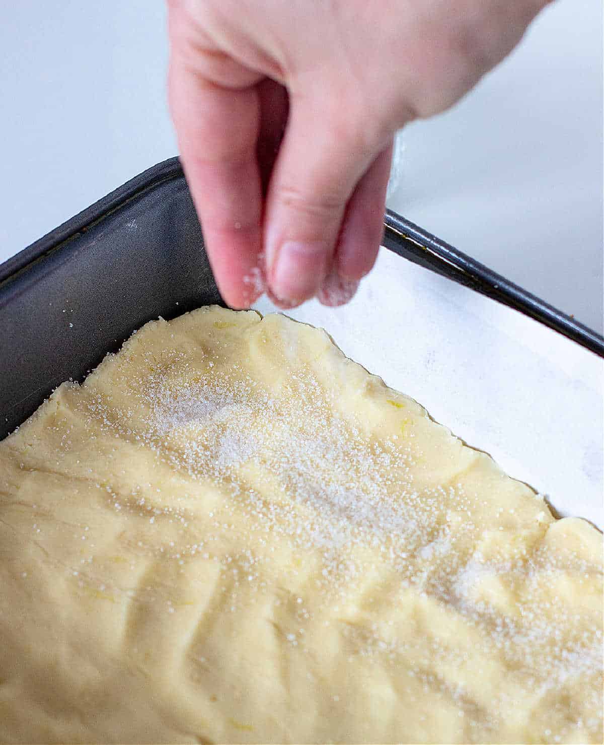 Hand sprinkling sugar on the unbaked shortbread base.