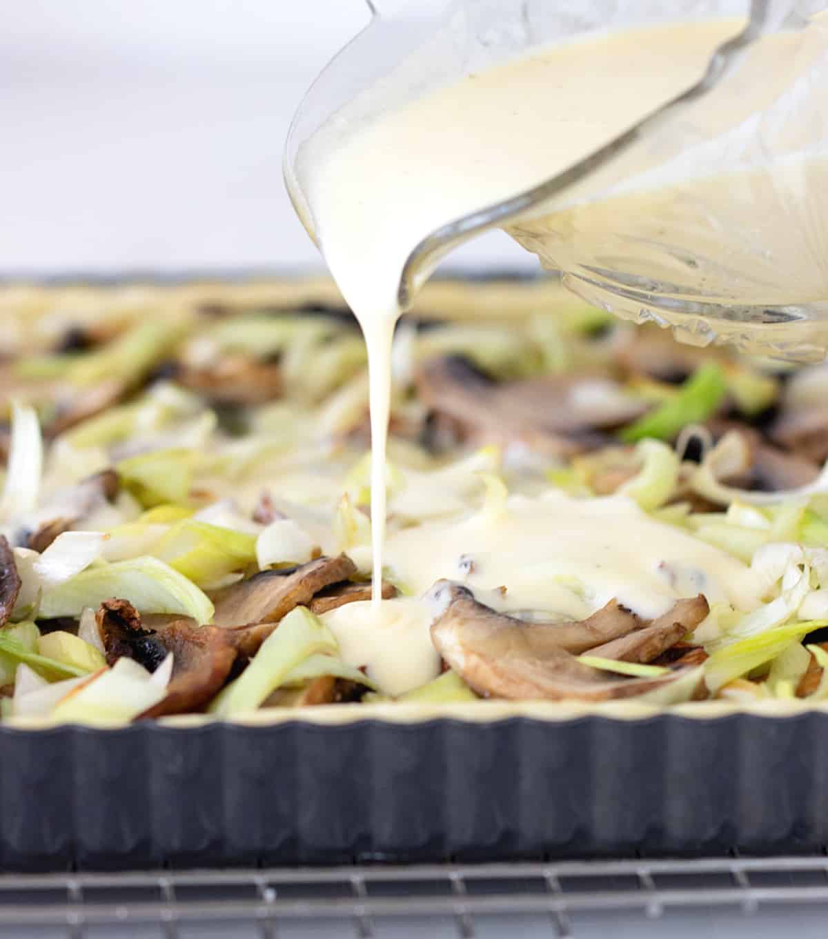 Pouring of binding cream over mushroom quiche filling
