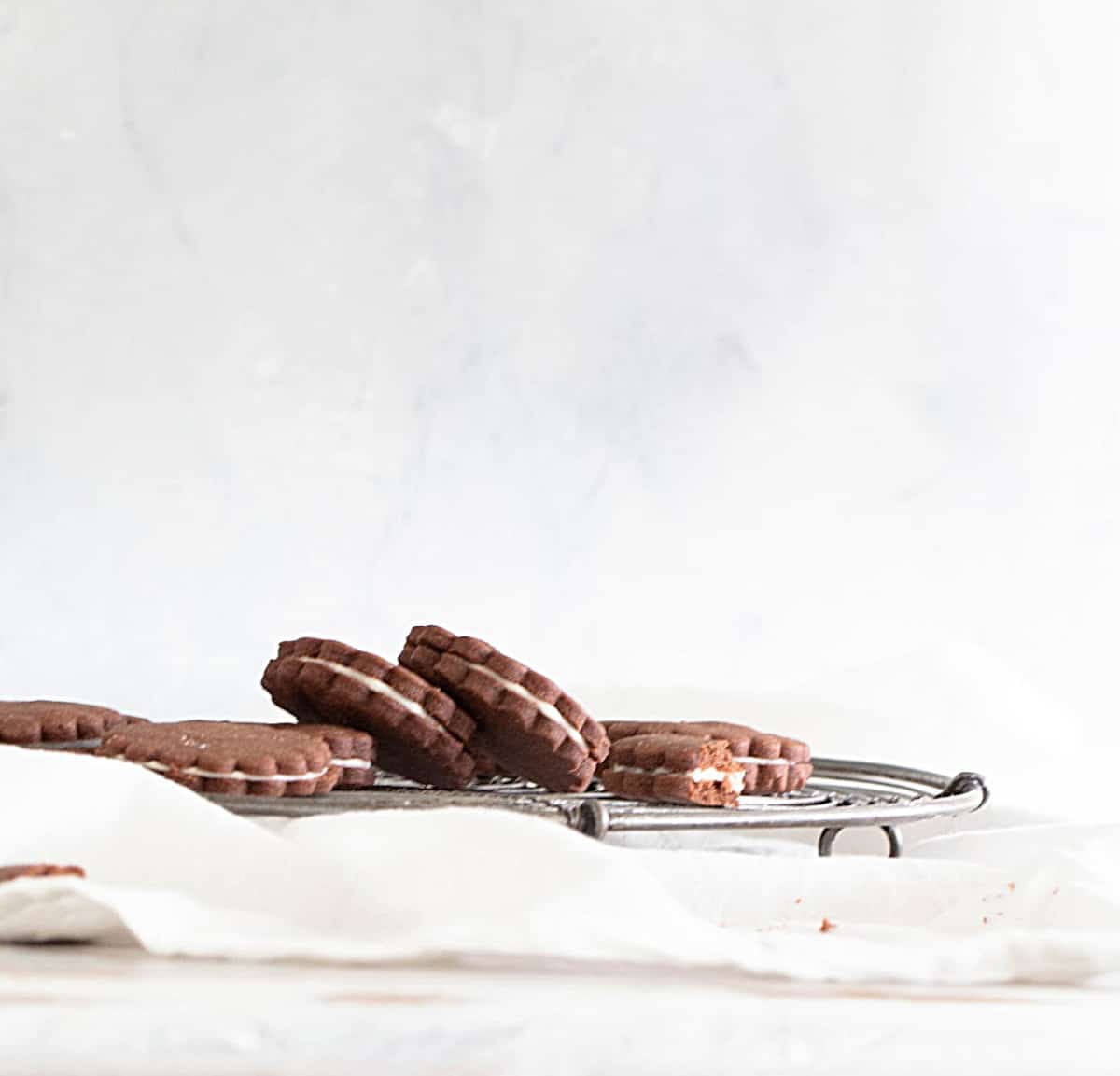 Several chocolate sandwich cookies on metal wire rack, white background