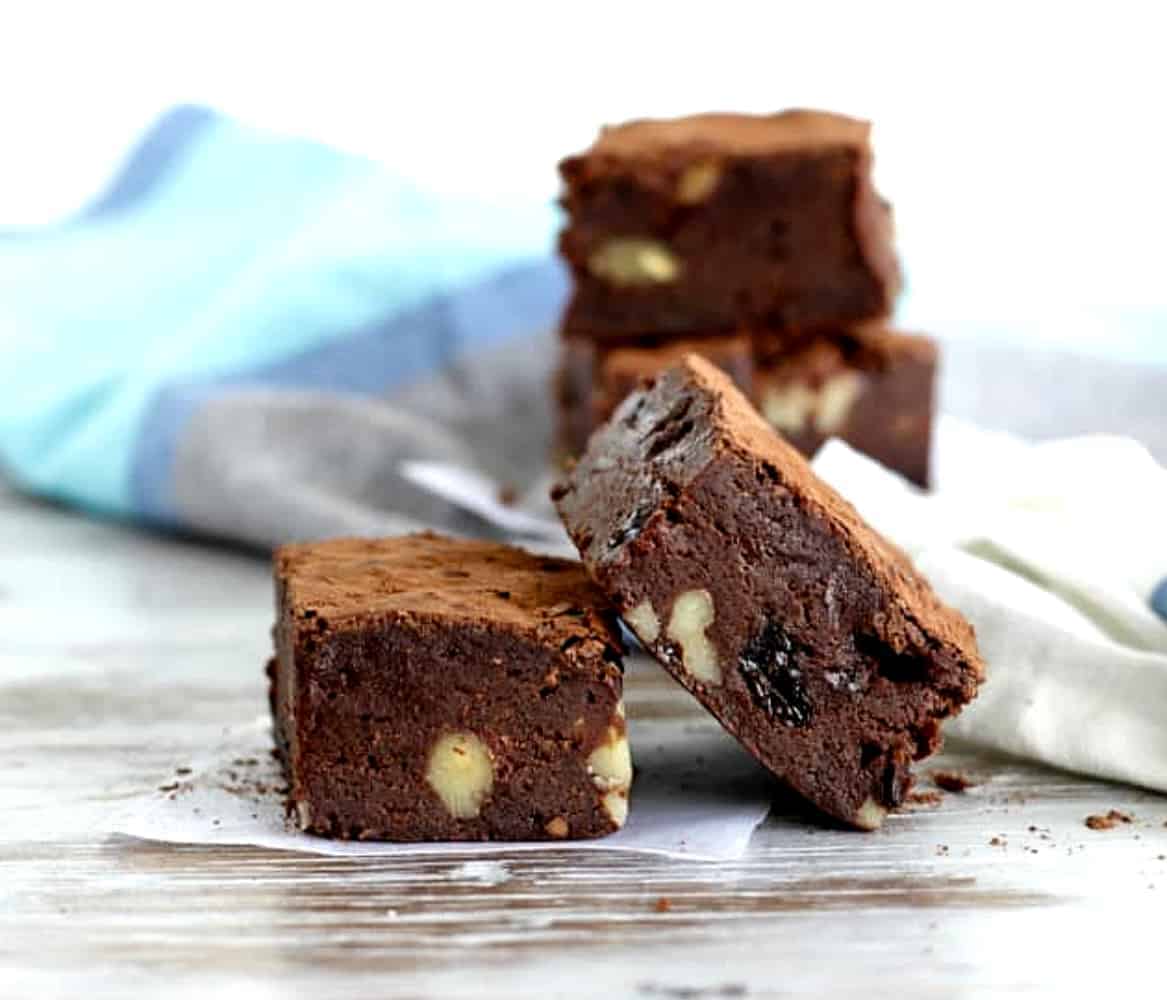 Walnut raisin brownie squares on white surface, blue grey cloth.