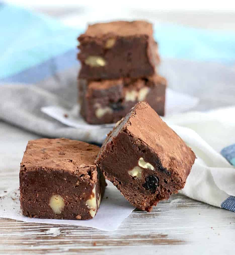 Walnut raisin brownie squares on white surface, blue grey cloth