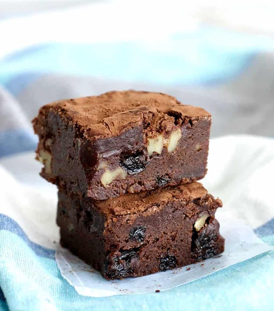 Stack of two walnut raisin brownies on blue grey cloth