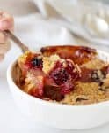 Spoon lifting apple blackberry crumble from white bowl