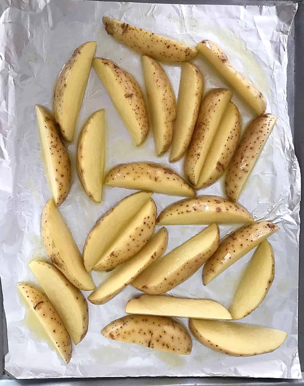 Oiled raw potato wedges on aluminum paper