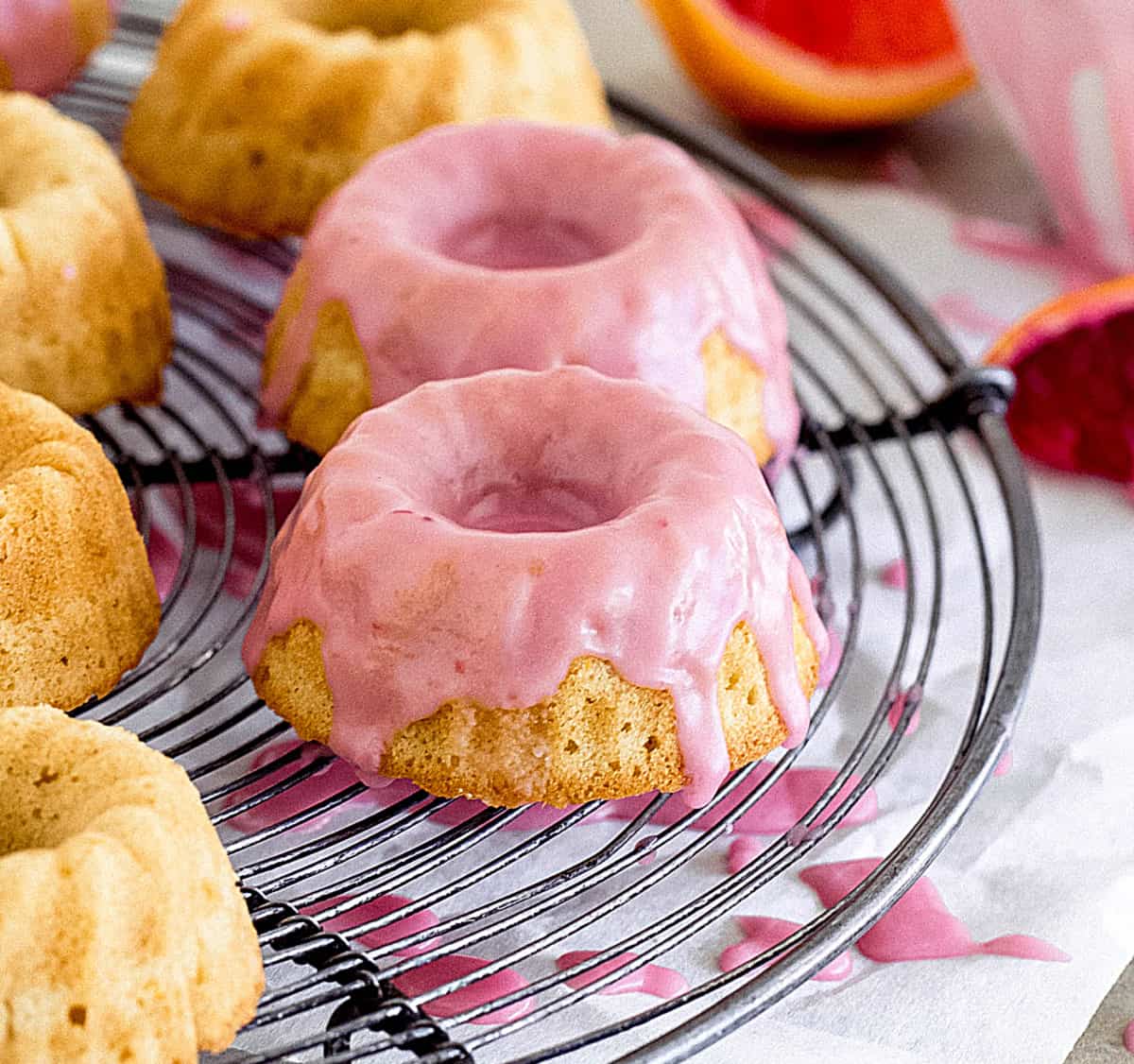 Close-up of mini cake with pink glaze on a round grey wire rack