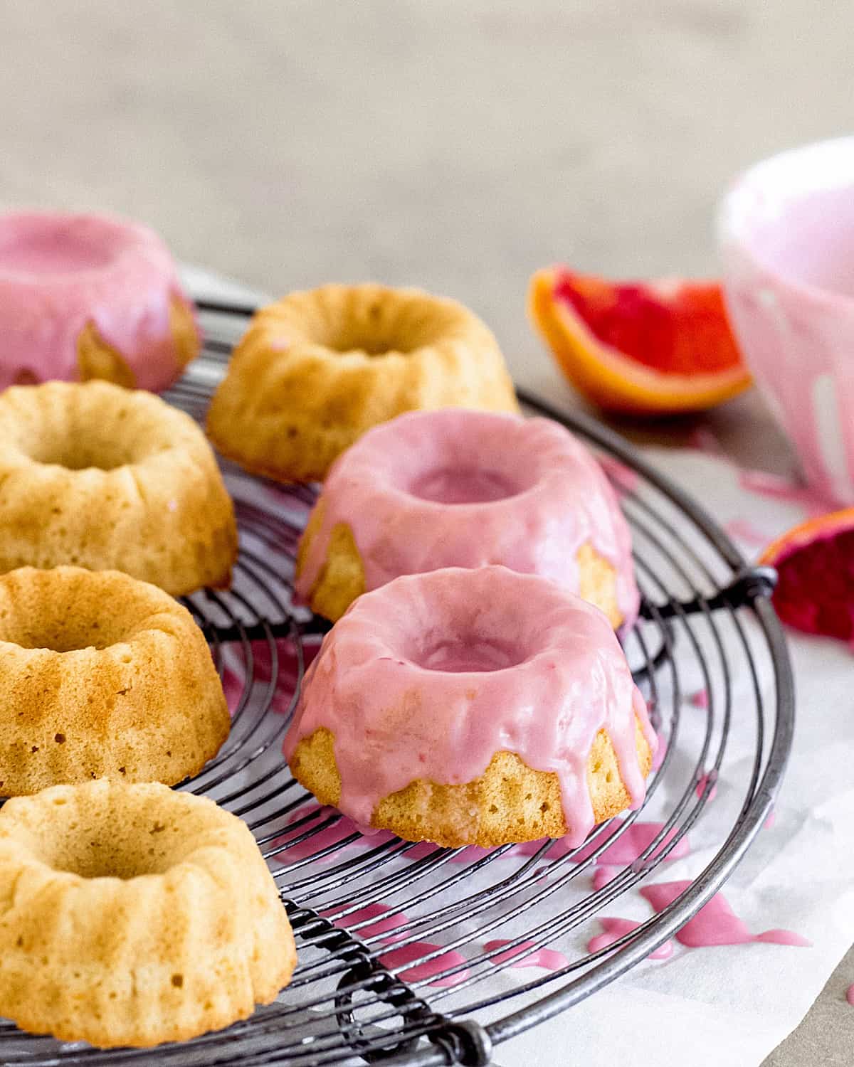 Mini cakes on wire rack with pink glaze, blood orange wedges beside