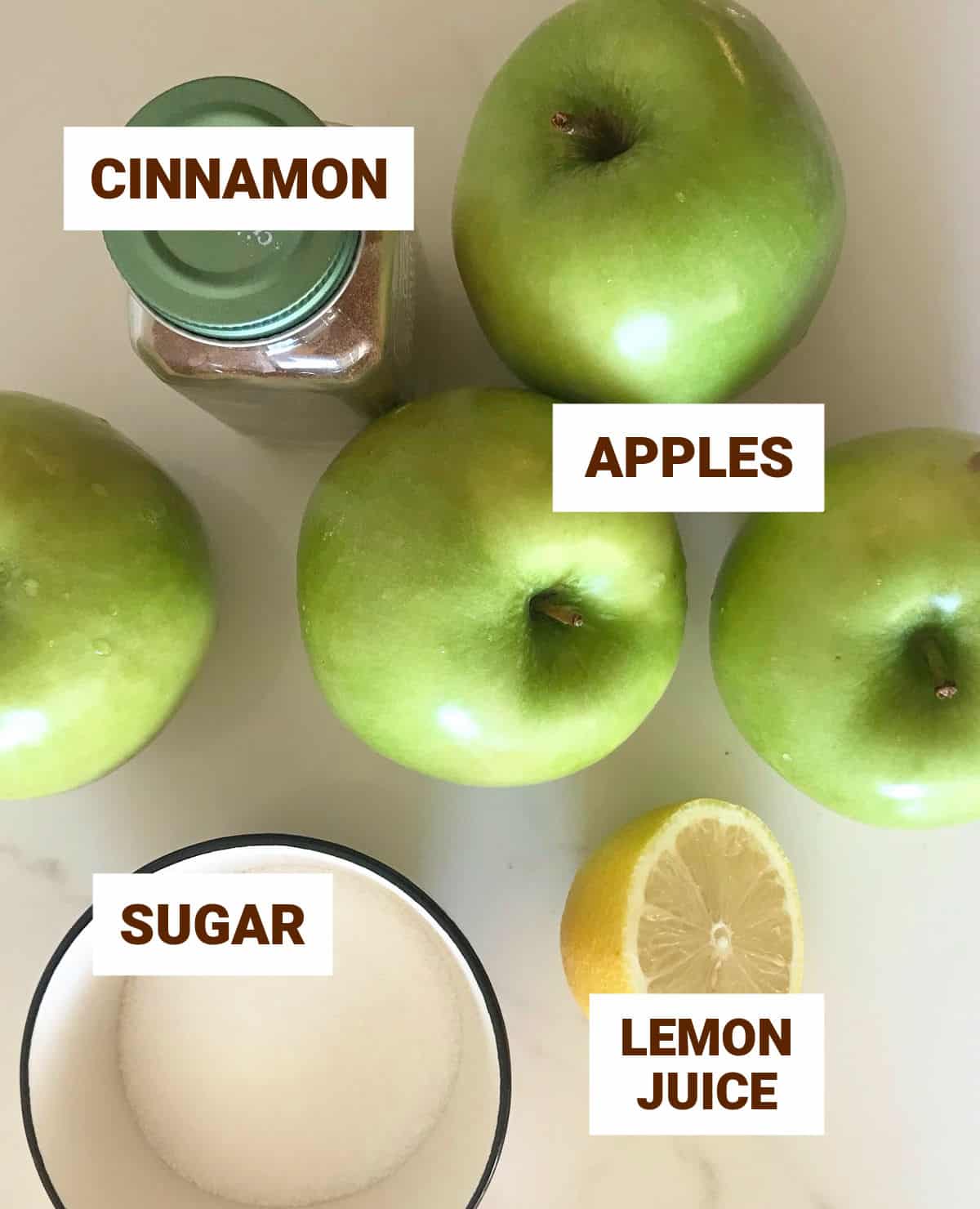 Green apples, half a lemon, and other ingredients ingredients on white surface