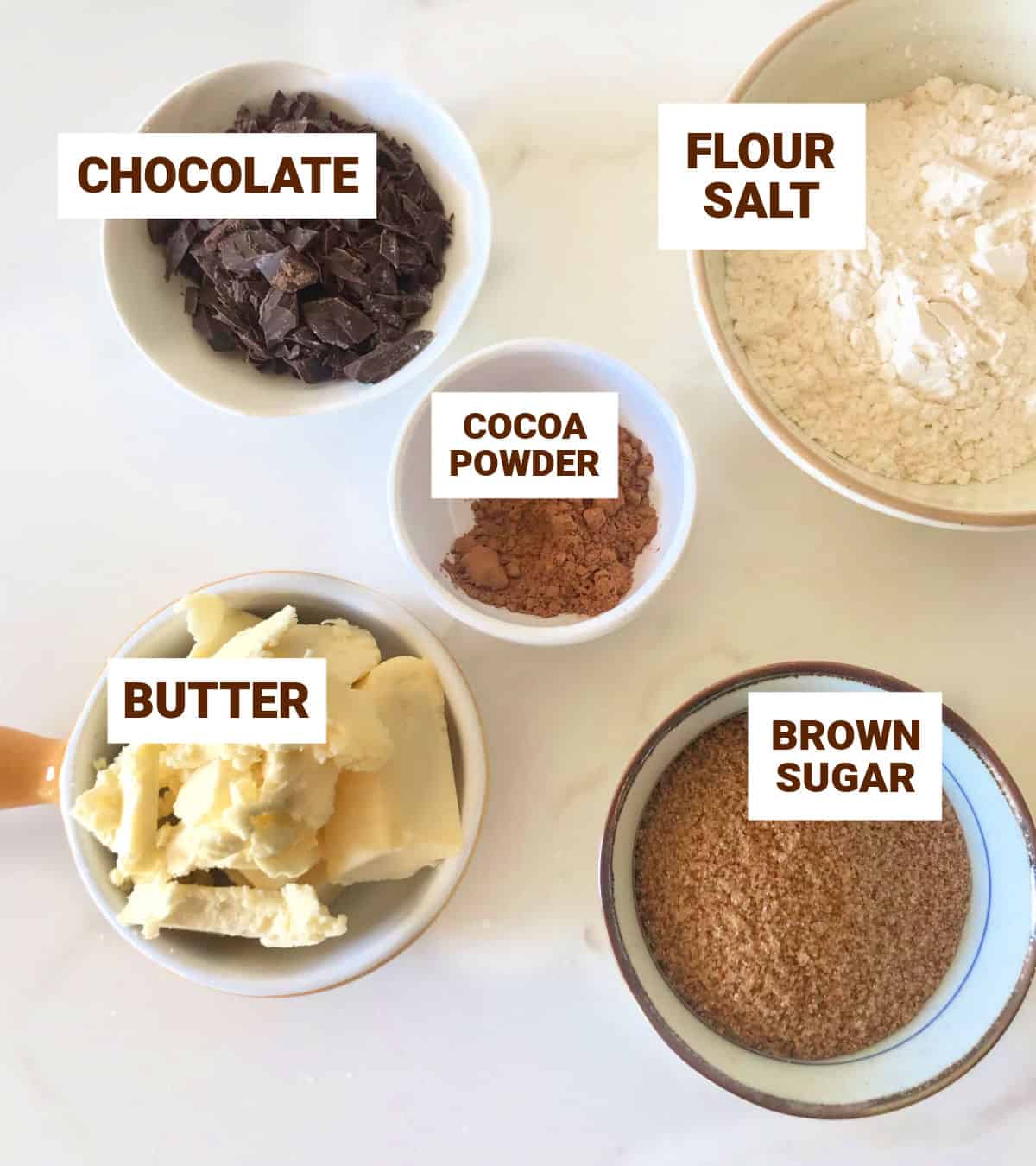 Chocolate crumble ingredients in different sized bowls on white surface