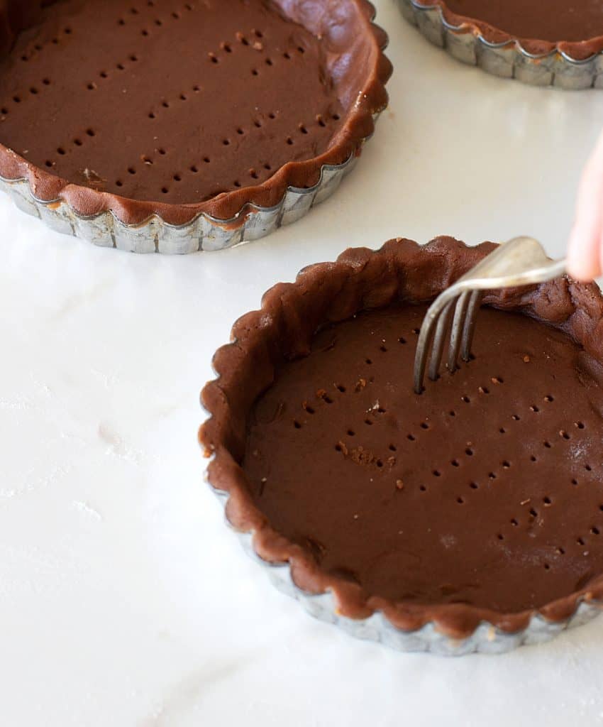 Pricking chocolate tart crusts with fork, white counter