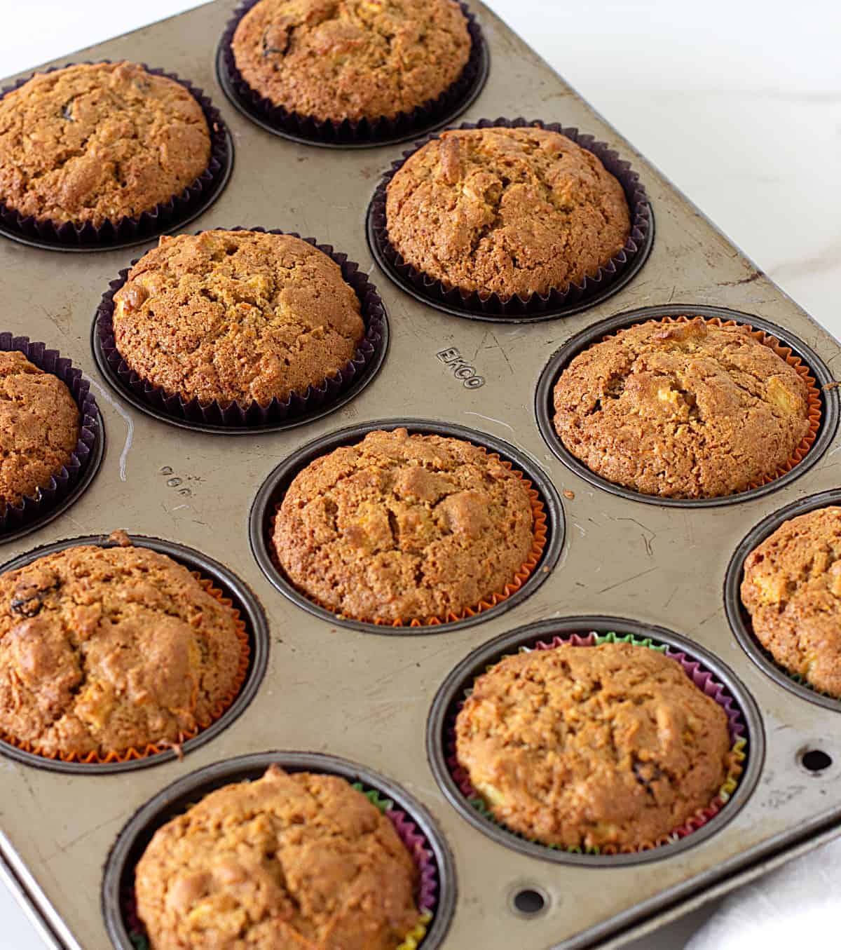 A large metal muffin pan with baked muffins in paper liners