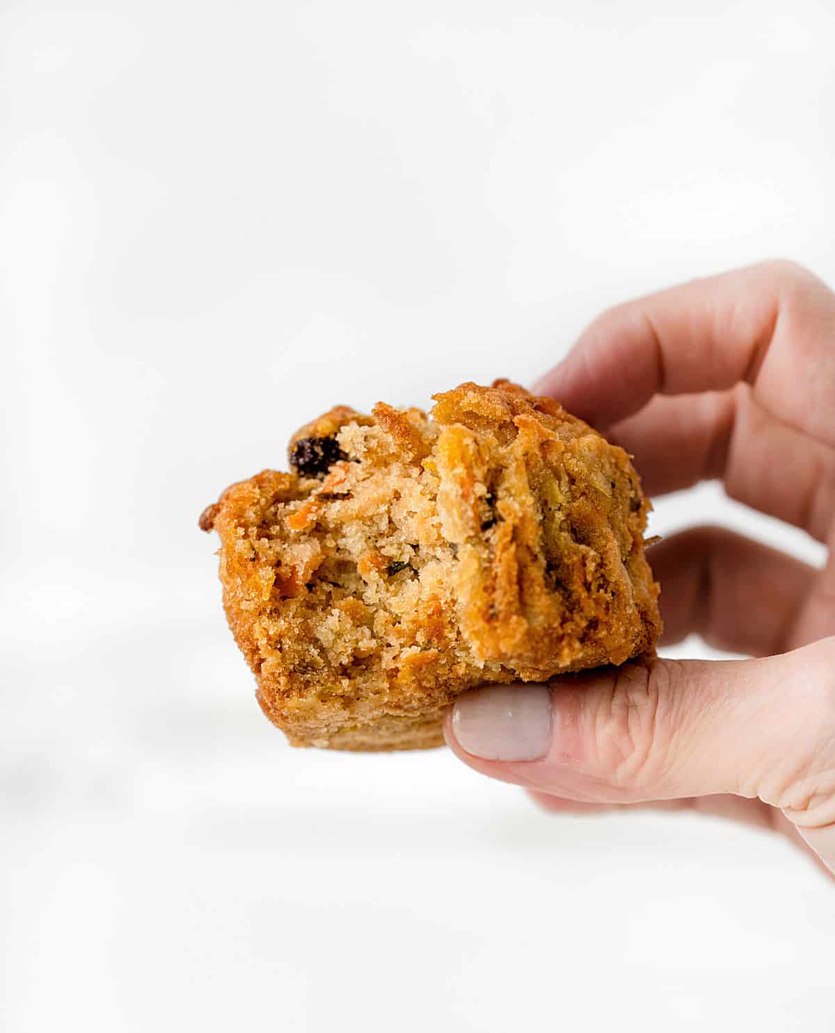 Hand holding a bitten carrot raisin muffin with a white background.