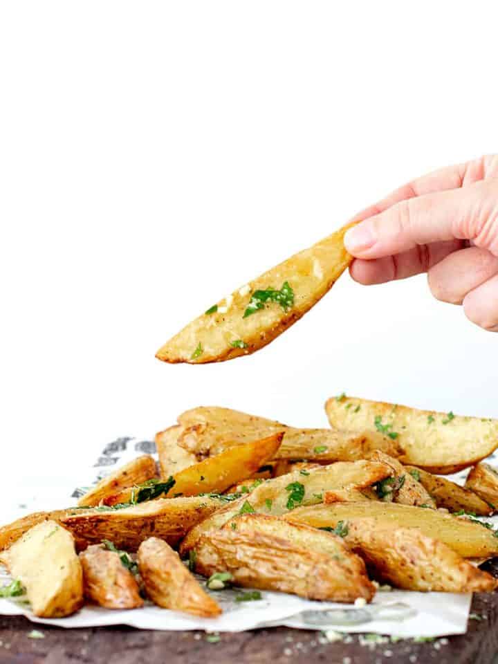 Hand holding potato wedge beneath a mound of potato wedges on a wooden board