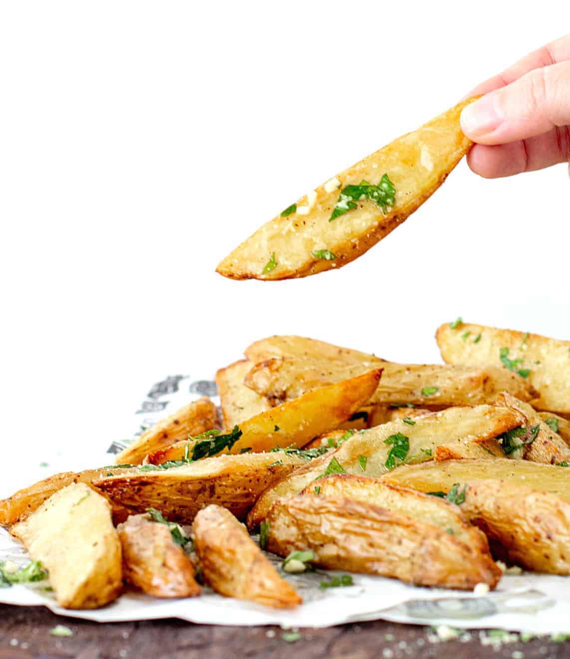 Hand holding potato wedge beneath a mound of potato wedges on a wooden board